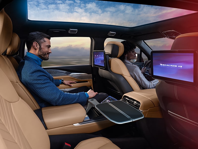 A Man Sitting in the 2025 ESCALADE IQ Back Seat Utilizing the Second Row Features