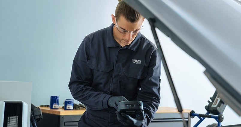 Cadillac Certified Service Technician Typing Information Into a Device While Standing Next to a Vehicle