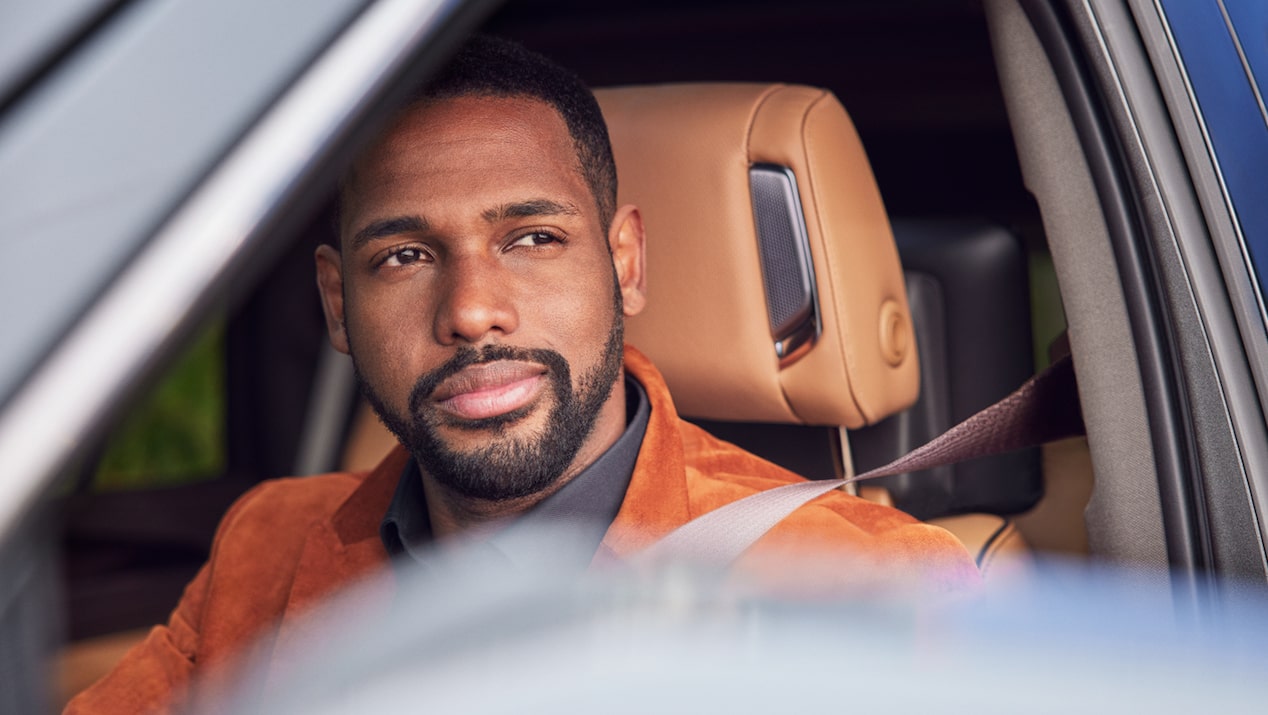 Man sitting in the driver’s seat of a Cadillac Escalade. He’s looking out the window and smiling.