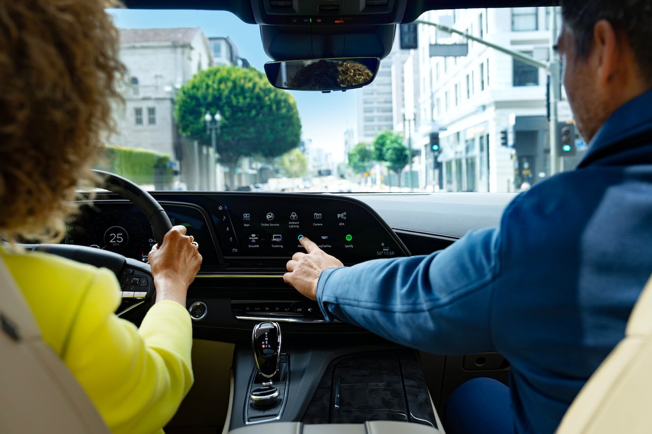 Back Seat View of a Lady Driving a Cadillac and the Passenger Utilizing the InVehicle Apps on the Display Screen