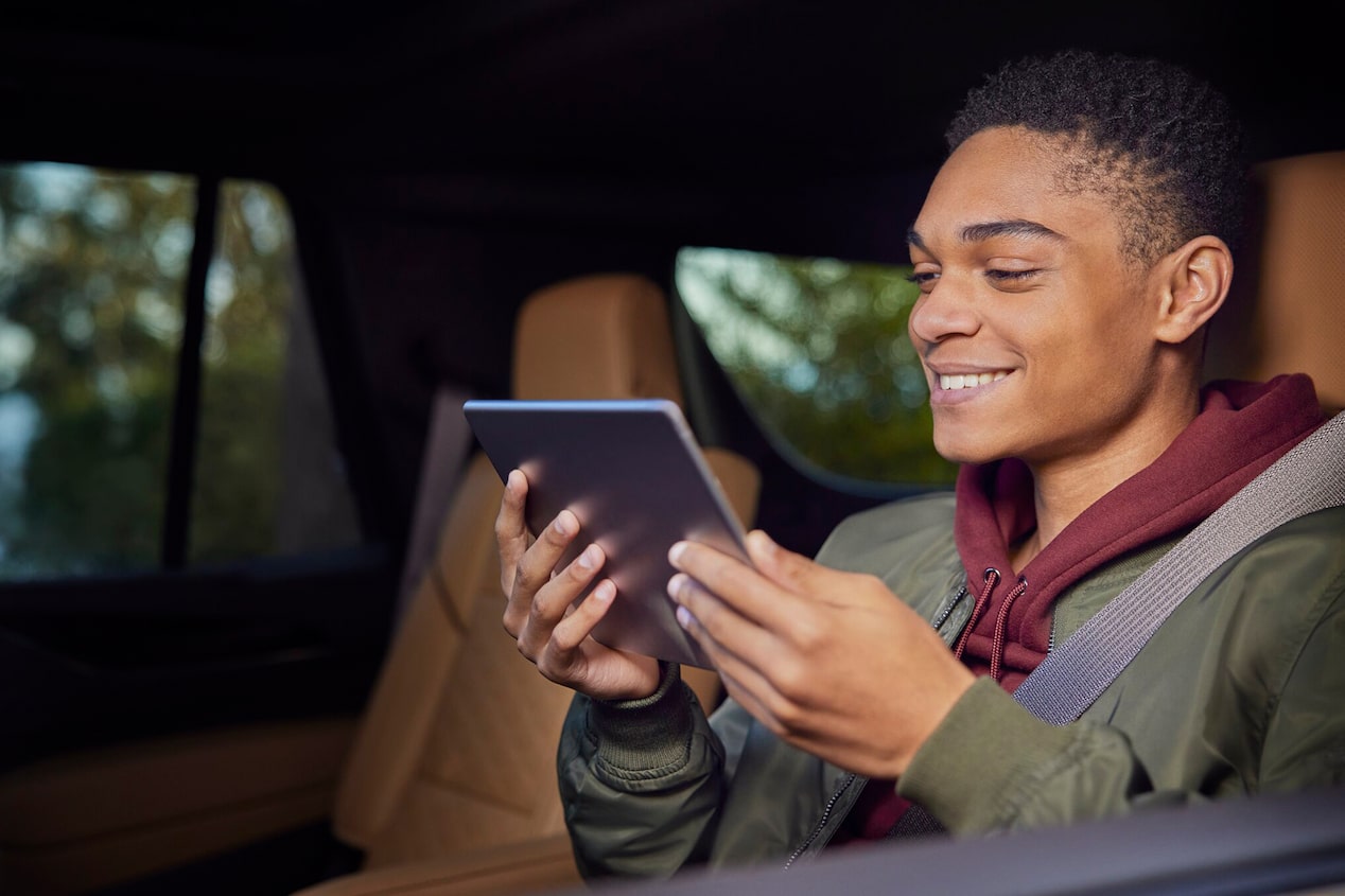 A Young Man Smiling While Holding and Looking at an iPad in the Back Seat