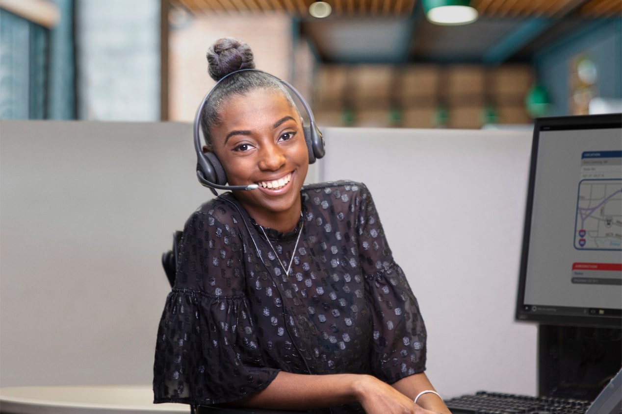 A Woman Smiling With a Headset on and at Her Desk