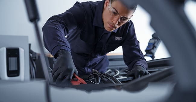 Cadillac Technician Attaching Jumper Cables to a Vehicle's Battery