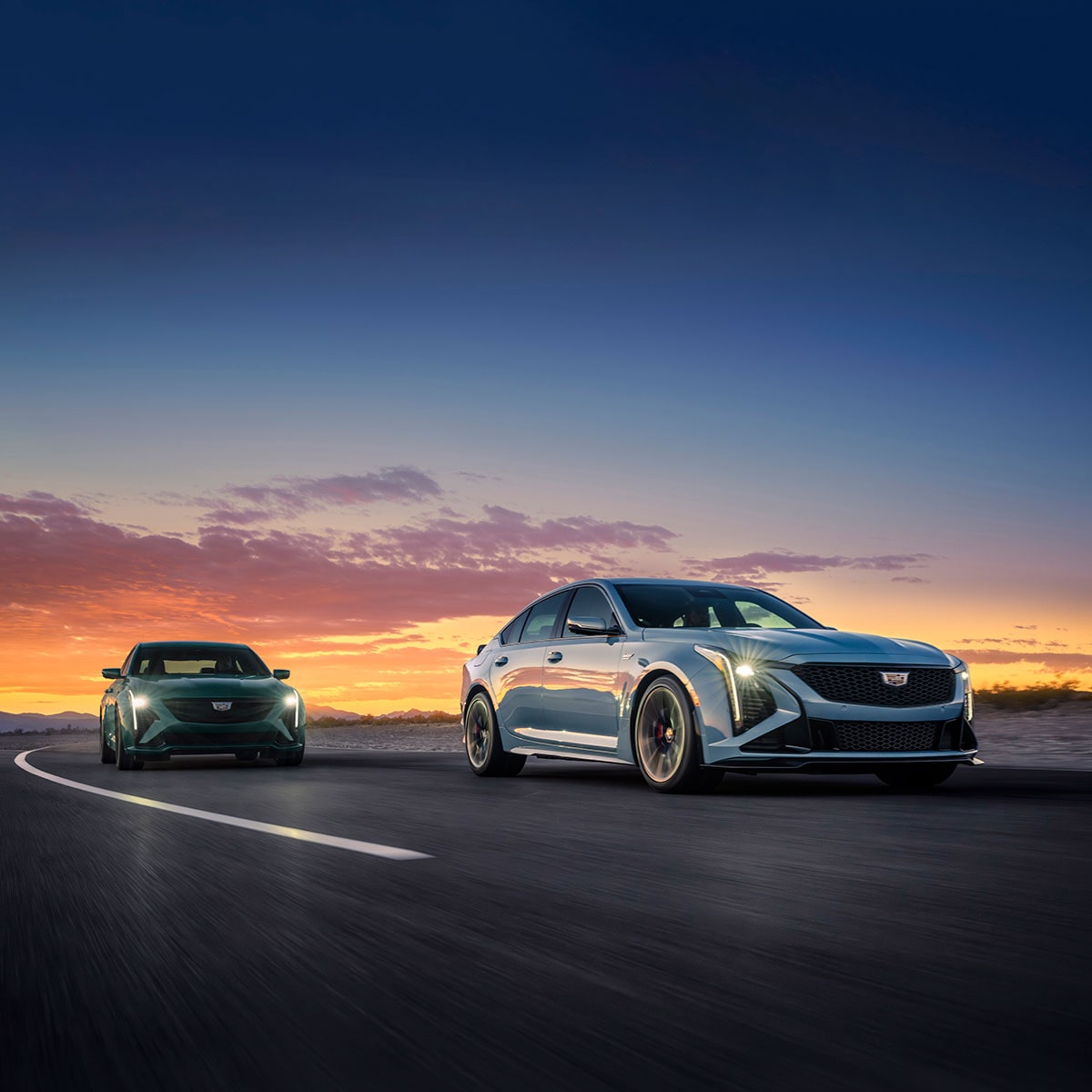 Front View of Two White and Green Cadillac CT5 V-Series Driving Down the Road During a Sunset