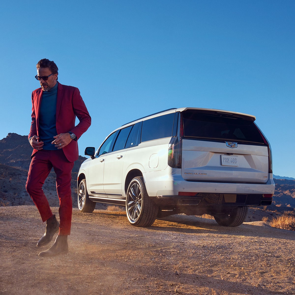 A Fashionable Dressed Man Walking Away From a White Cadillac Escalade in the Desert