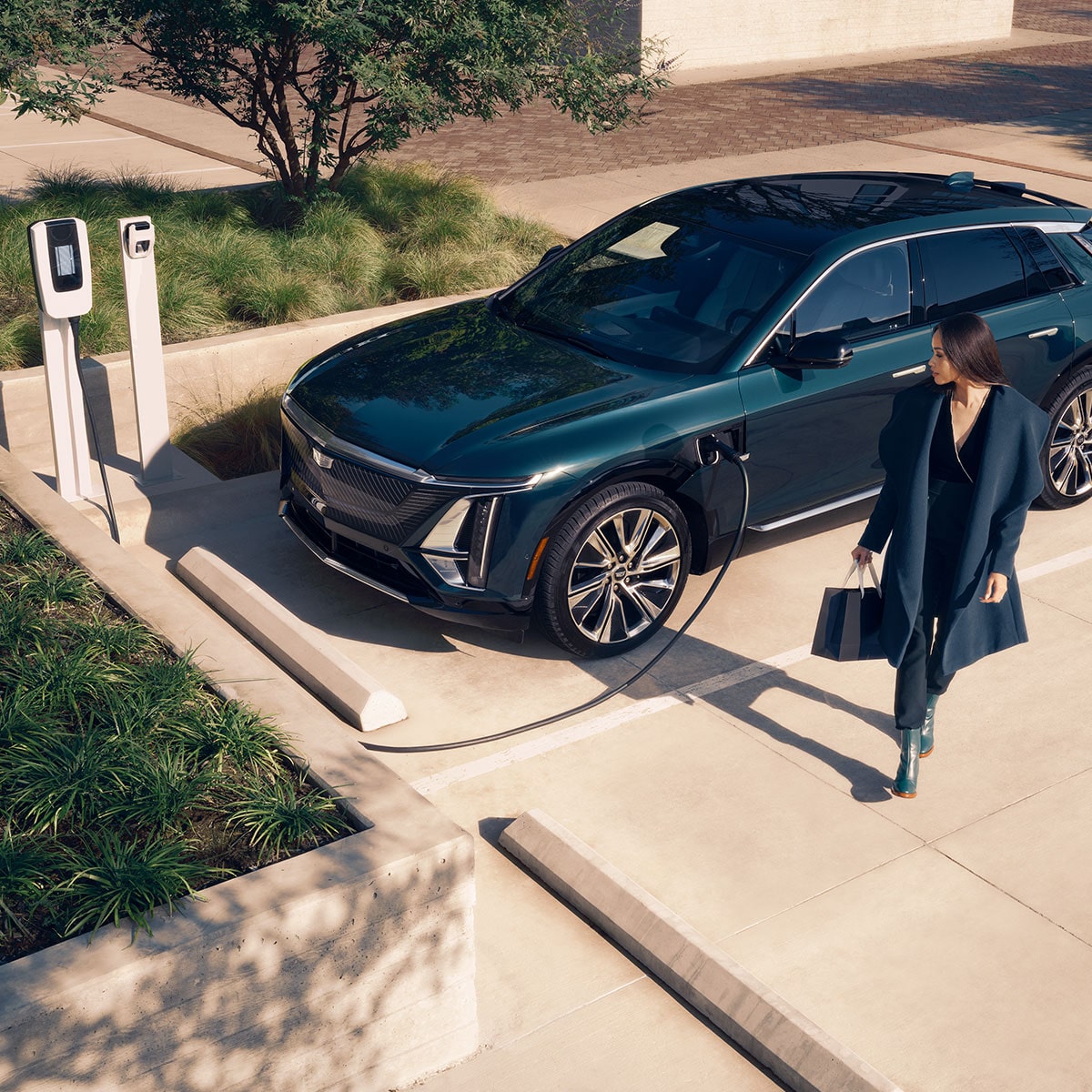 Three-Quarters View of a Woman Walking Away from a Parked 2026 LYRIQ-V Charging at a Public Charger