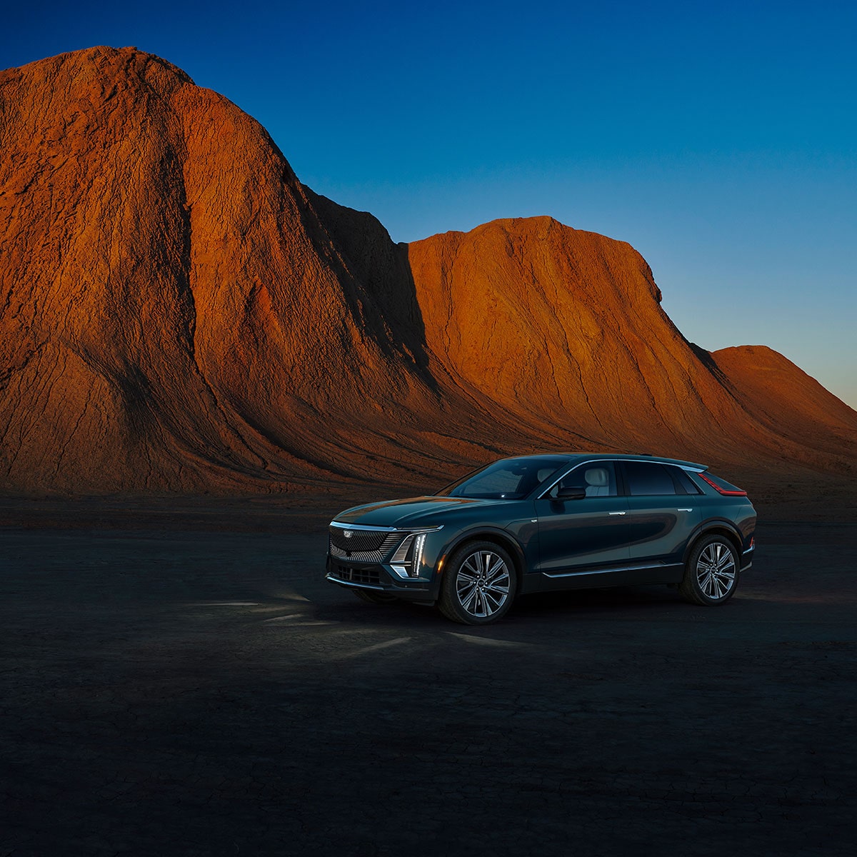 The LYRIQ Parked in a Gravel Field with A Mountain Backdrop in the Near Distance