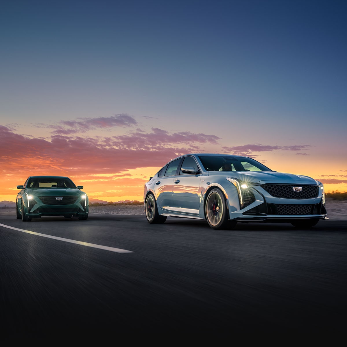 Two 2025 Cadillac CT5-V Sedans Driving on a Road Under an Evening Sky